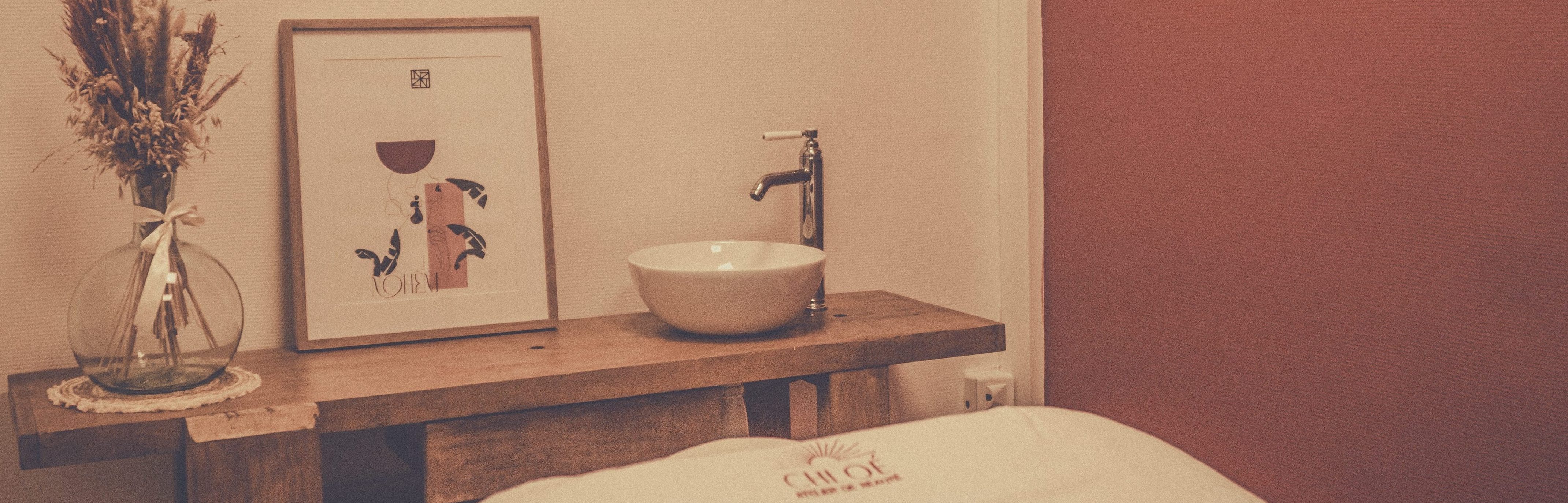 Photographie représentant une partie de la salle de massage, on y voit un établi servant de vasque ainsi que des fleurs séchées. L'ambiance est chaleureuse.